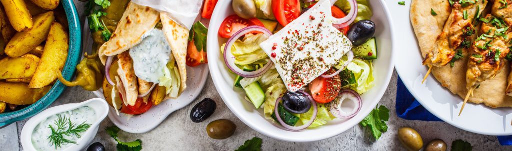 Greek food: greek salad, chicken souvlaki, gyros and baked potato wedges on gray background, top view. Traditional greek cuisine concept.